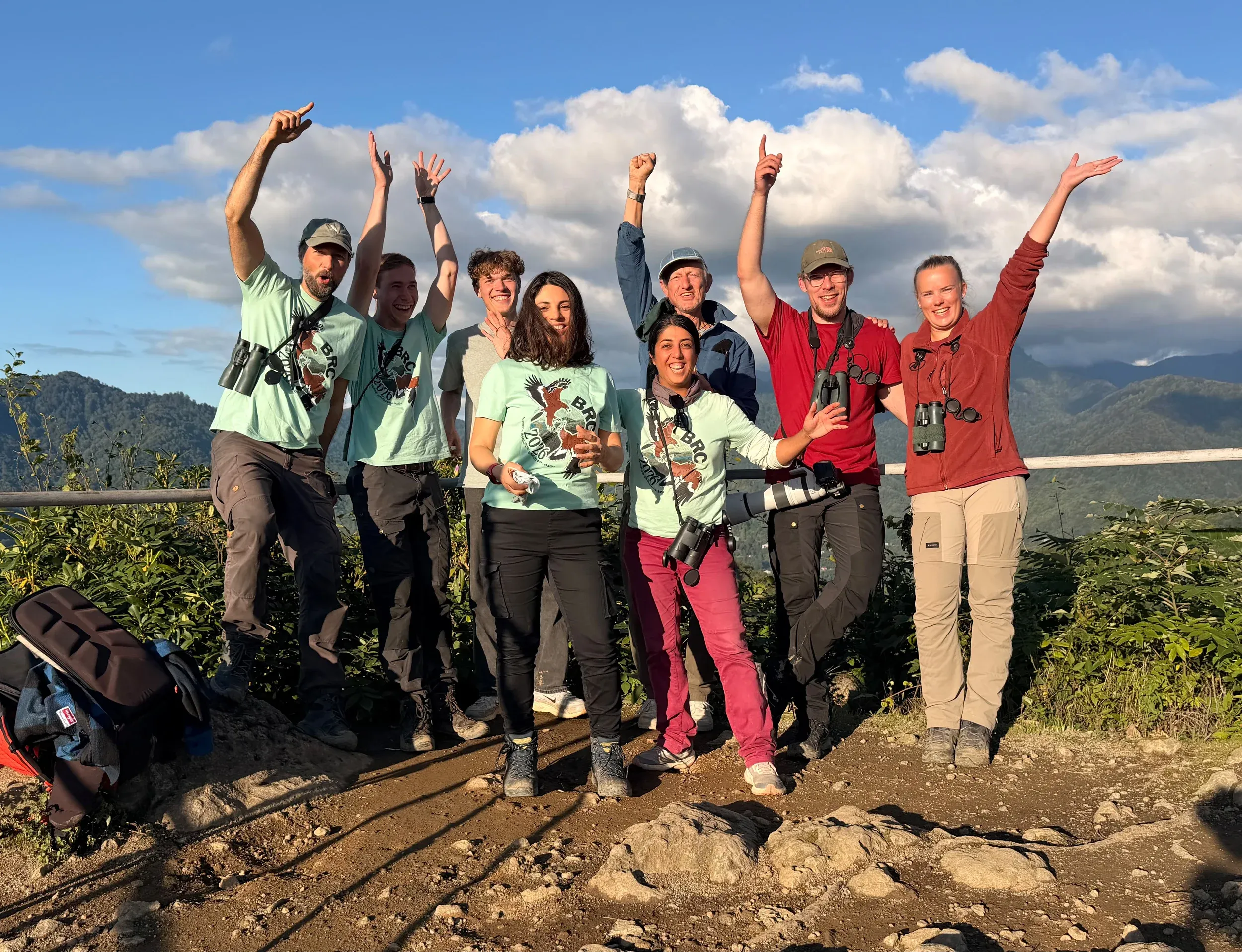 The Station 2 team smiling and raising their arms at the count station, with green hills behind them.
