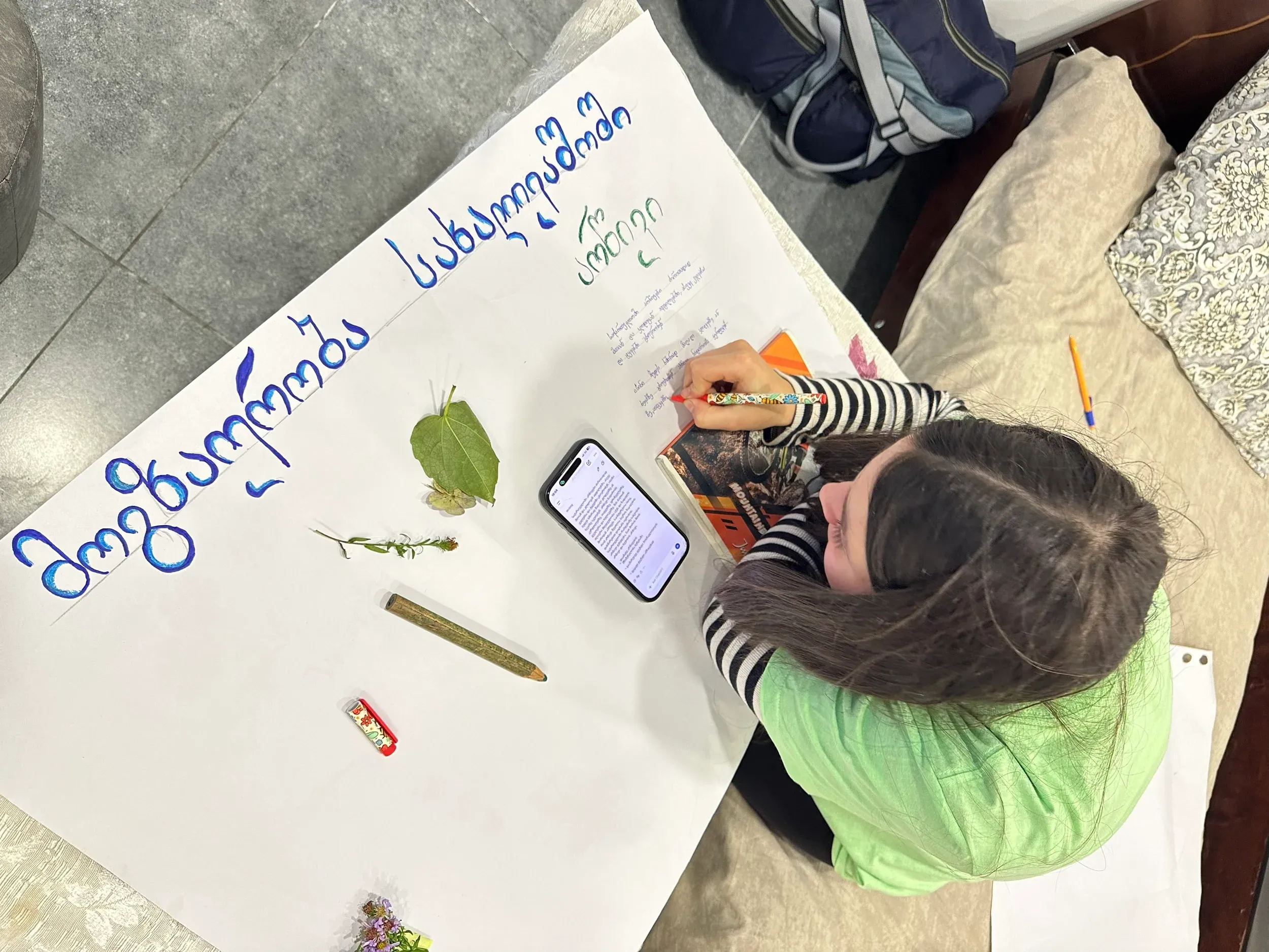 A student writing on a large poster decorated with leaves and flowers