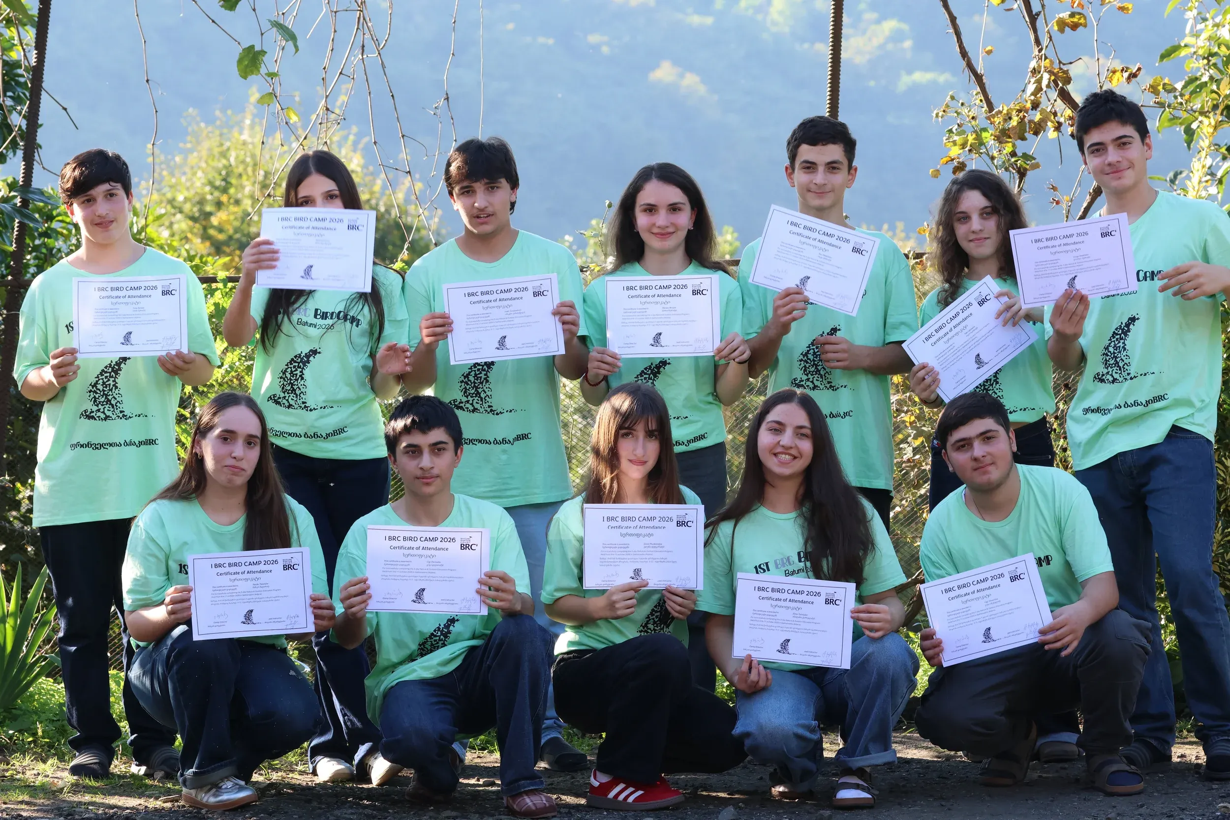 Bird camp participants in green T-shirts holding their certificates