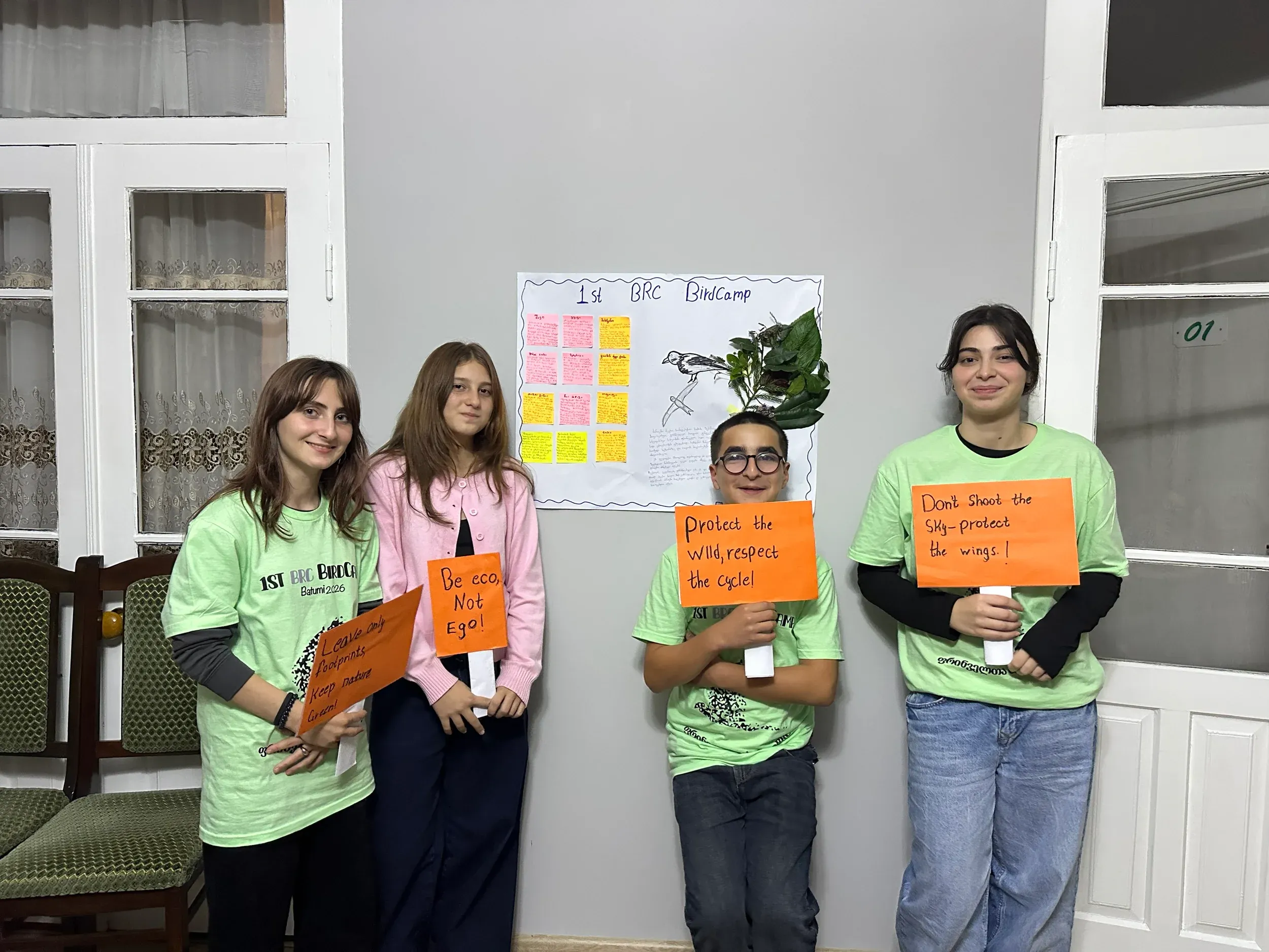 Four students holding handwritten conservation messages in front of their bird camp poster